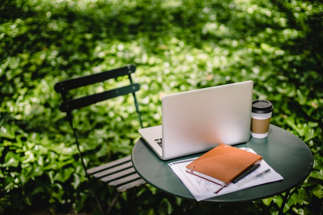 cozy table with laptop, notebook, and coffee cup in park.