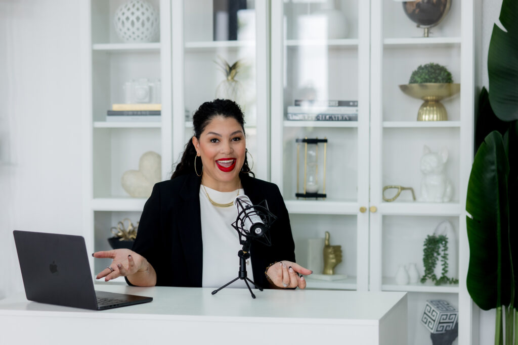 Heidy de la cruz sitting in front of her microphone taling baout Podcast Coaching for Established Shows